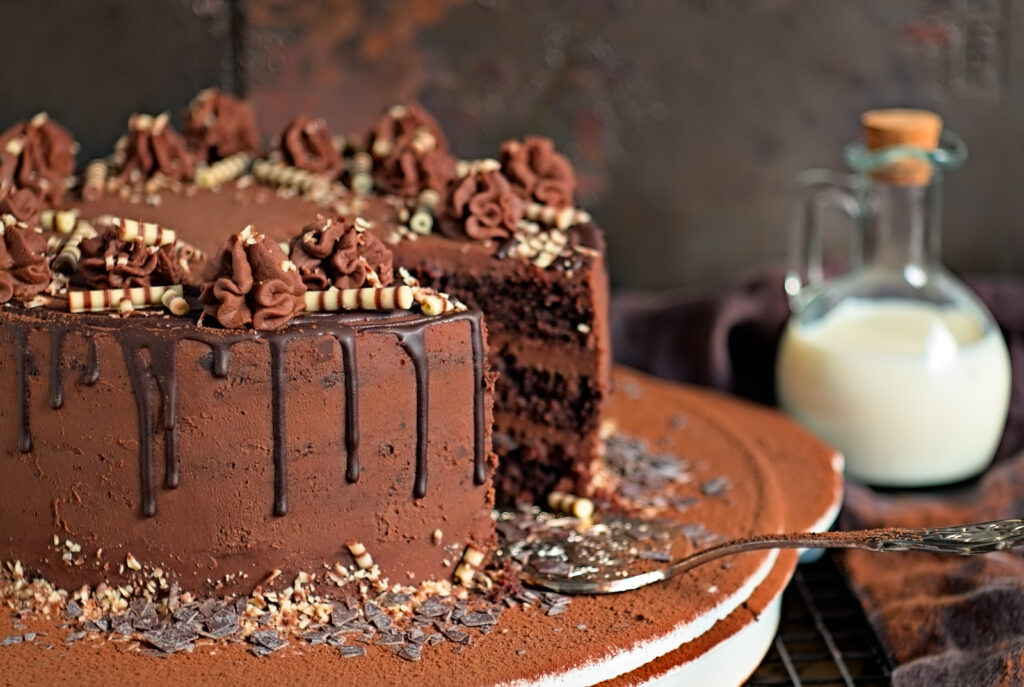angeschnittene Schokoladentorte auf einer Tortenplatte, verziert mit Sahnehäubchen und Schokoladendeko
